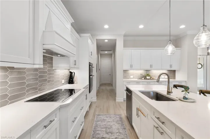 Kitchen with white cabinetry, light wood-style flooring, backsplash, light stone countertops, and ornamental molding