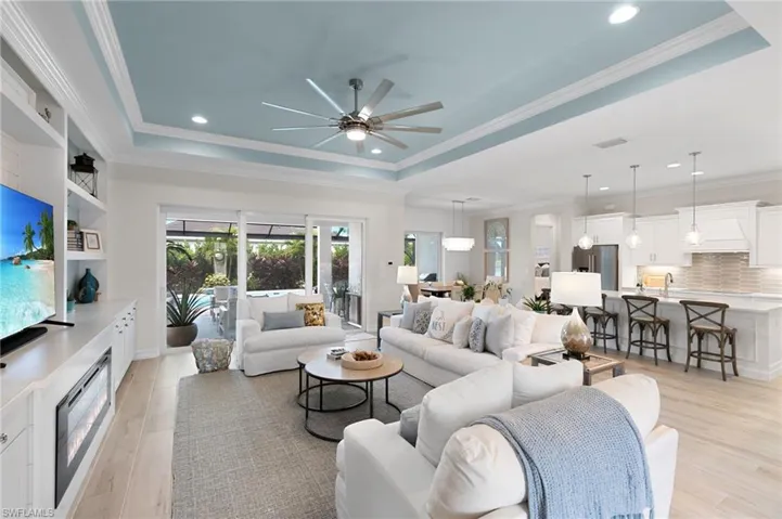 Living area with a tray ceiling, crown molding, recessed lighting, ceiling fan, and light wood-type flooring