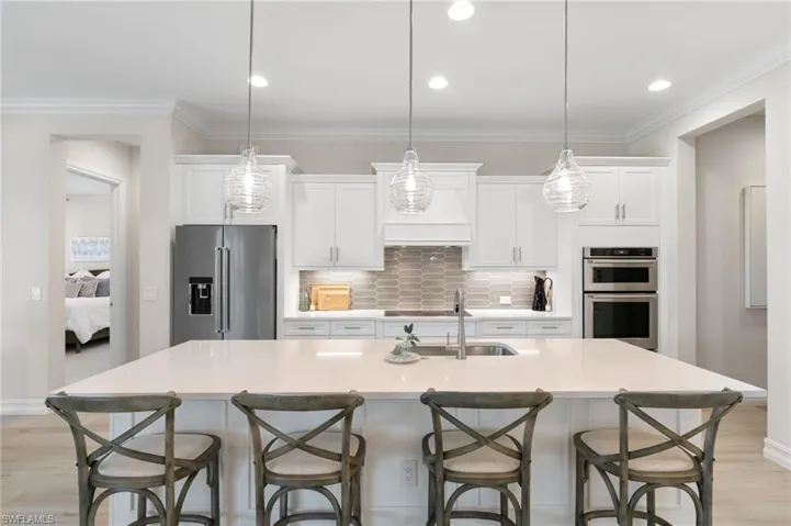 Kitchen featuring light wood-style flooring, white cabinetry, appliances with stainless steel finishes, backsplash, and ornamental molding