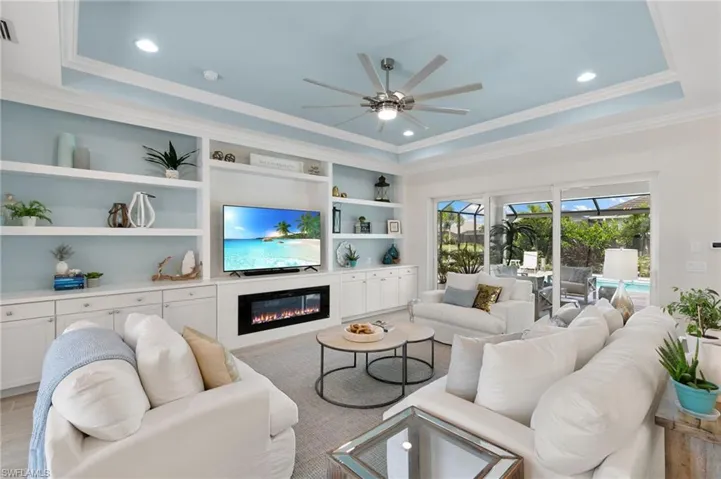 Living area featuring a tray ceiling, light wood-style flooring, crown molding, ceiling fan, and a glass covered fireplace