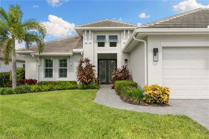 View of exterior entry featuring stucco siding, a garage, a lawn, and a tiled roof