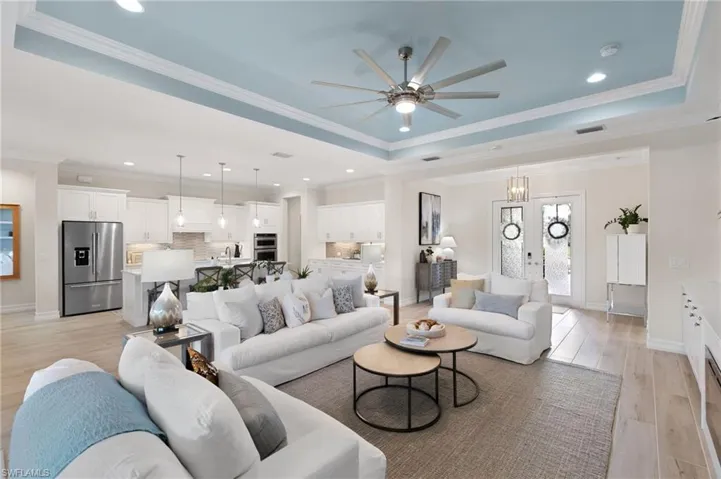 Living room featuring a tray ceiling, ornamental molding, light wood finished floors, recessed lighting, and a ceiling fan