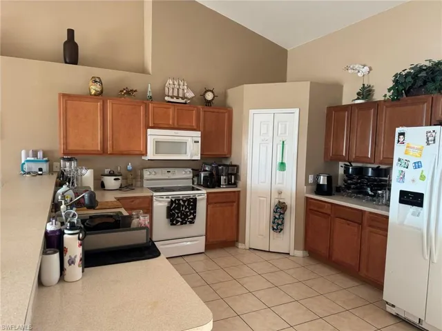 Kitchen featuring white appliances, light tile patterned floors, light countertops, and high vaulted ceiling