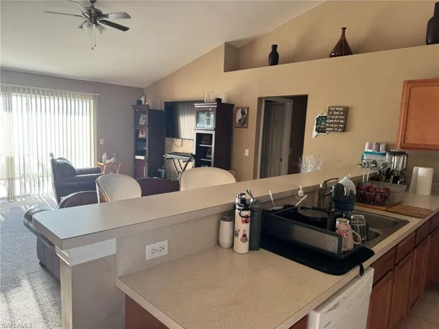 Kitchen with a sink, light countertops, lofted ceiling, and white dishwasher