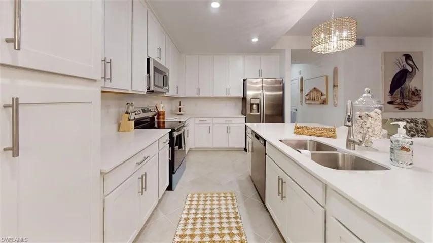 Kitchen with stainless steel appliances, white cabinets, decorative light fixtures, light stone countertops, and recessed lighting