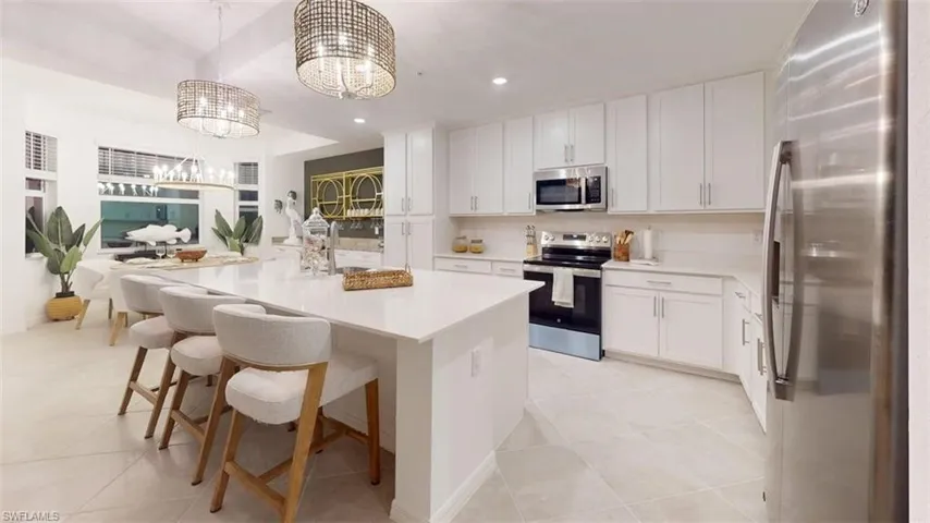 Kitchen with appliances with stainless steel finishes, white cabinets, a kitchen island with sink, a breakfast bar area, and hanging light fixtures