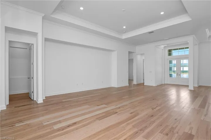 Unfurnished living room featuring crown molding, a tray ceiling, french doors, and light wood-type flooring