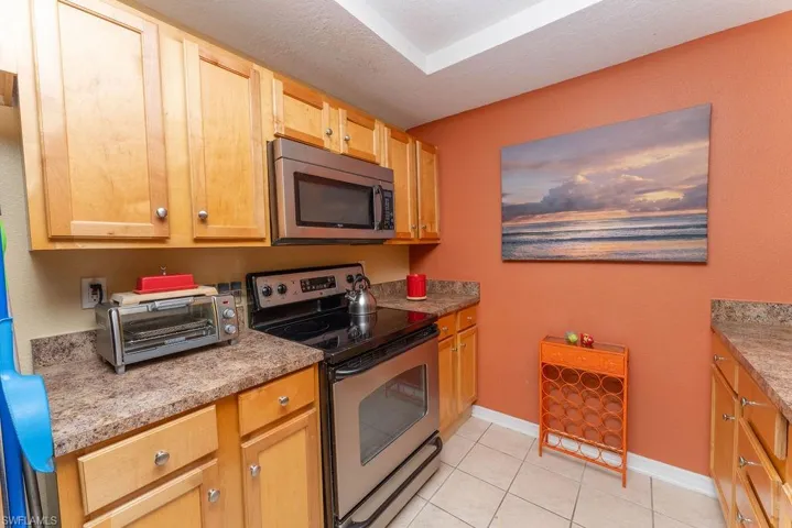 Kitchen with appliances with stainless steel finishes, light tile patterned floors, a textured ceiling, light brown cabinetry, and light countertops