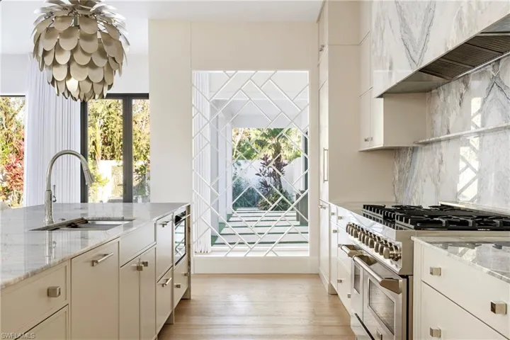 Kitchen with custom exhaust hood, double oven range, sink, light stone countertops, and a wealth of natural light