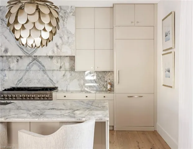 Kitchen with light stone countertops, decorative backsplash, light hardwood / wood-style flooring, and stainless steel gas stovetop