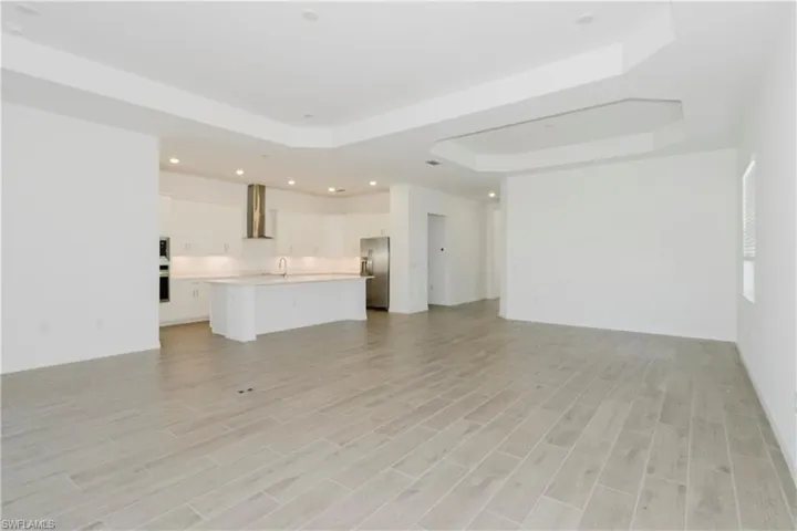 Unfurnished living room with recessed lighting, a sink, a raised ceiling, and light wood-style floors