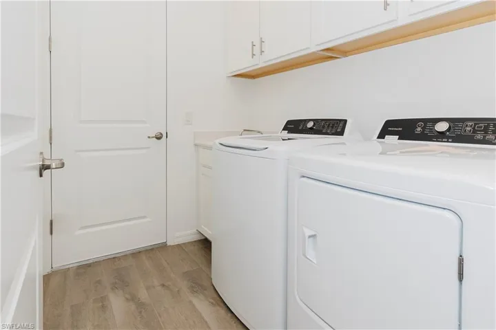 Washroom featuring light wood-style floors, cabinet space, and washing machine and clothes dryer