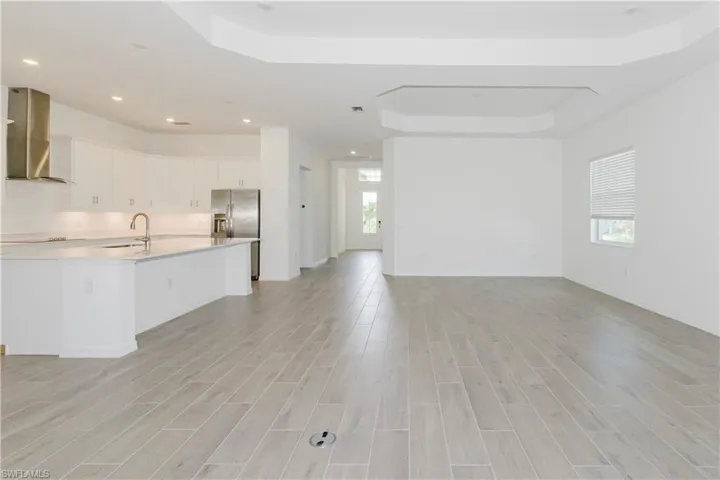 Kitchen featuring wall chimney range hood, a sink, stainless steel fridge with ice dispenser, open floor plan, and a tray ceiling