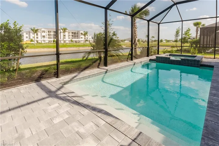 View of swimming pool with glass enclosure, a water view, a pool with connected hot tub, and a patio