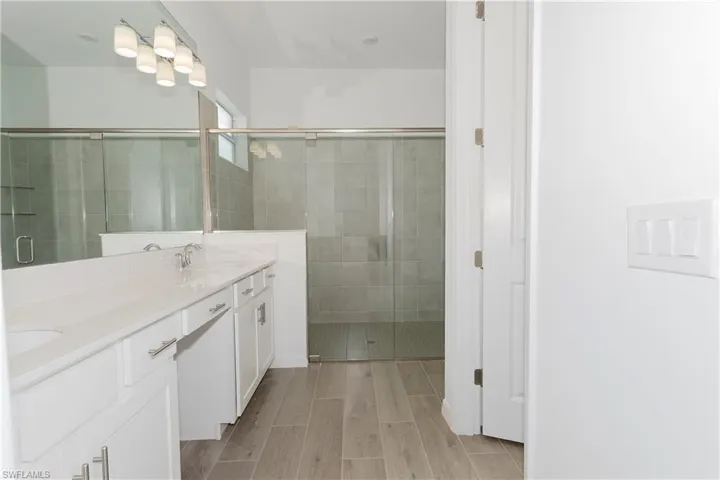 Bathroom featuring wood finished floors, double vanity, a sink, and a stall shower