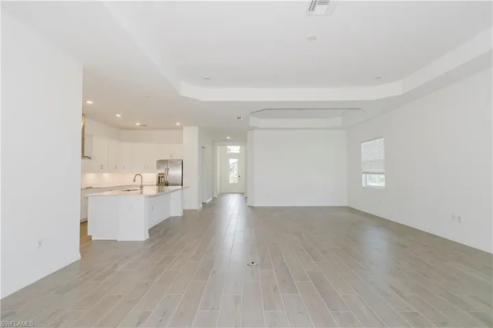 Unfurnished living room with a tray ceiling, visible vents, a sink, and light wood-style floors