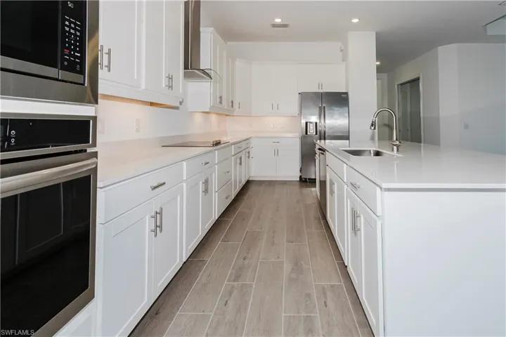 Kitchen with wall chimney range hood, light countertops, a sink, light wood-style flooring, and appliances with stainless steel finishes