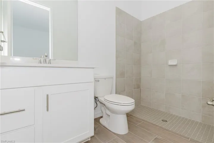 Bathroom featuring vanity, a tile shower, toilet, and wood finished floors