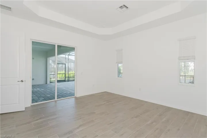 Empty room featuring visible vents, light wood-style flooring, and a raised ceiling