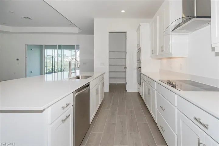 Kitchen with a sink, light countertops, wall chimney exhaust hood, stainless steel appliances, and recessed lighting