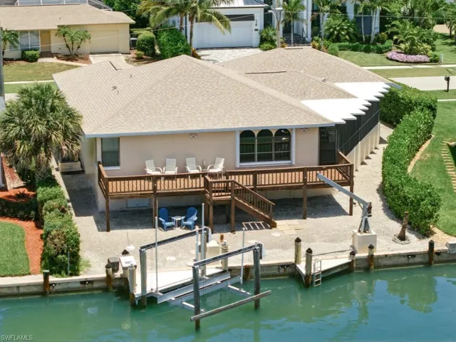 Rear view of property featuring a shingled roof, boat lift, a deck, stucco siding, and stairs