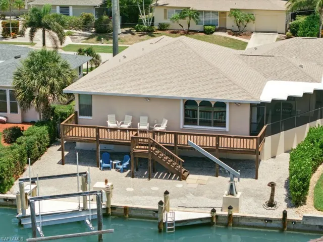Back of property with roof with shingles, stucco siding, boat lift, and a wooden deck