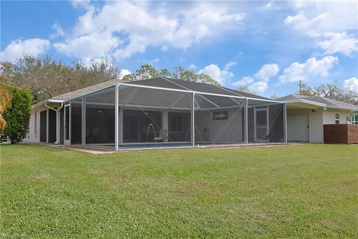Back of property featuring an outdoor pool, a lanai, and a lawn