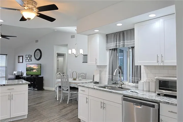 Kitchen with light stone counters, white cabinets, stainless steel dishwasher, lofted ceiling, and a ceiling fan