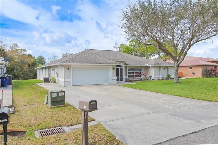 Ranch-style home featuring a front lawn, an attached garage, driveway, roof with shingles, and stucco siding