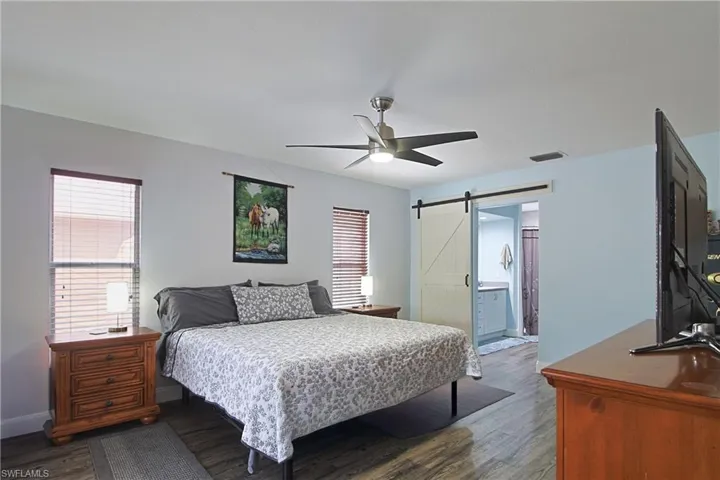 Bedroom featuring a barn door, dark wood-type flooring, ceiling fan, and connected bathroom