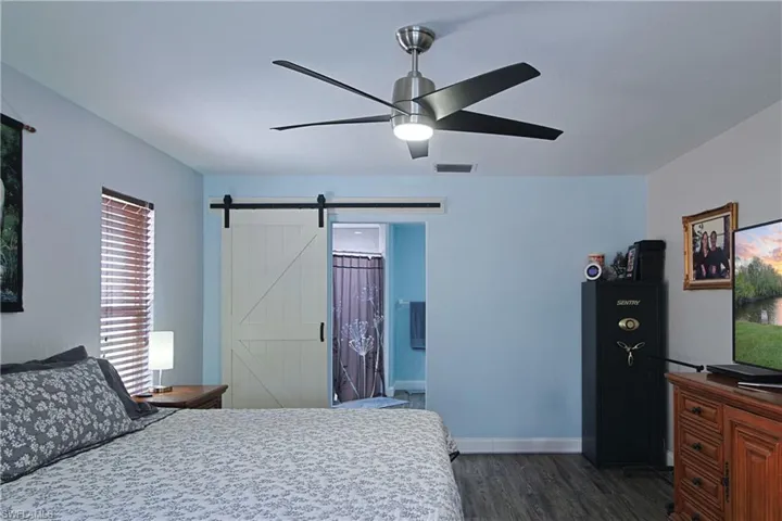 Bedroom featuring ensuite bath, a ceiling fan, dark wood-style floors, and a barn door