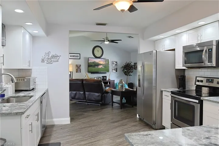 Kitchen featuring decorative backsplash, recessed lighting, light stone countertops, stainless steel appliances, and white cabinetry