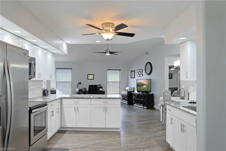 Kitchen with a peninsula, stainless steel appliances, light stone counters, white cabinetry, and recessed lighting
