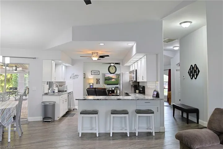 Kitchen featuring ceiling fan, light stone counters, a peninsula, backsplash, and recessed lighting