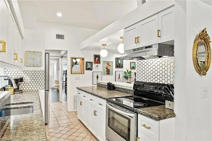 Kitchen featuring stainless steel range with electric stovetop, under cabinet range hood, tasteful backsplash, white cabinetry, and light tile patterned floors
