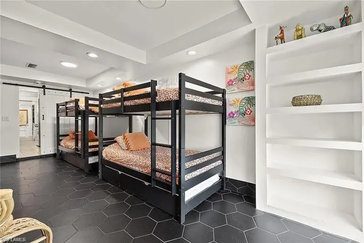 Bedroom featuring a barn door, a tray ceiling, recessed lighting, and dark tile patterned flooring
