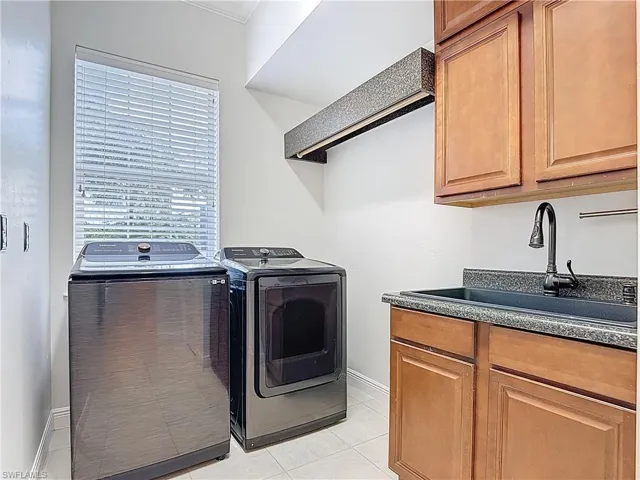 Washroom with cabinet space, washer and clothes dryer, and light tile patterned floors