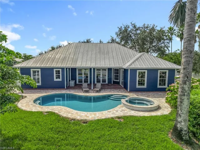 Rear view of house featuring a pool with connected hot tub, a patio, a metal roof, and a lawn