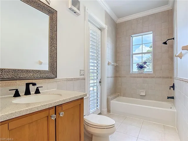 Full bath featuring bathing tub / shower combination, tile walls, vanity, ornamental molding, and light tile patterned floors