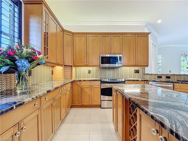 Kitchen featuring crown molding, dark stone countertops, brown cabinets, decorative backsplash, and appliances with stainless steel finishes