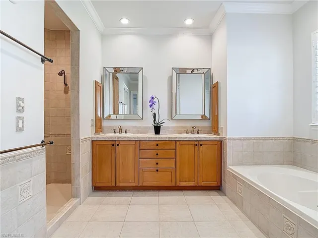 Full bathroom featuring crown molding, a garden tub, double vanity, tiled shower, and light tile patterned floors