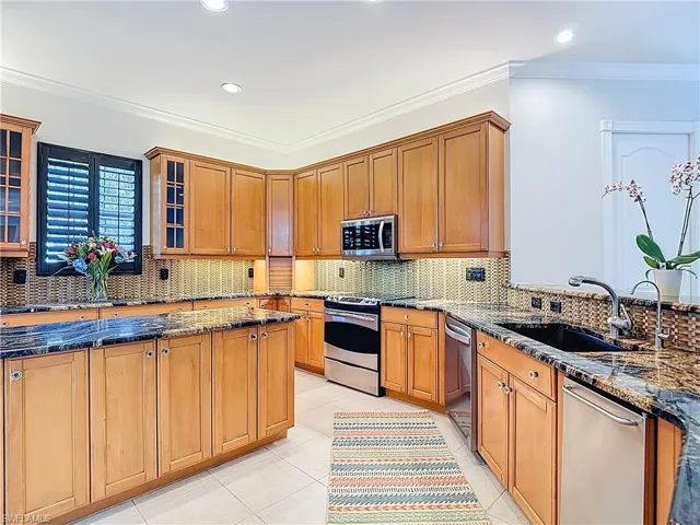 Kitchen featuring dark stone countertops, ornamental molding, decorative backsplash, brown cabinetry, and stainless steel appliances