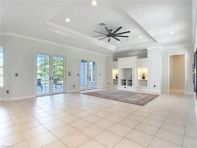 Unfurnished living room with french doors, a raised ceiling, ornamental molding, light tile patterned floors, and a ceiling fan