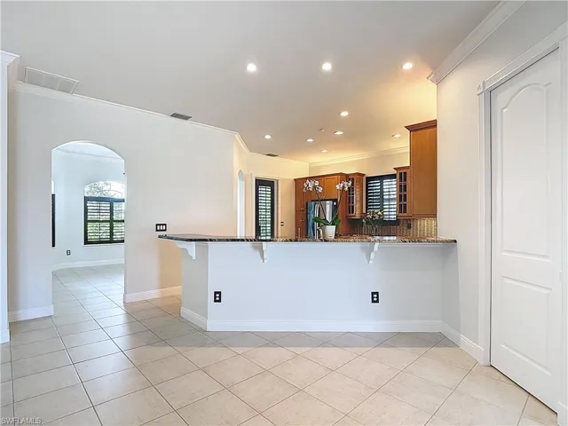 Kitchen with a breakfast bar area, crown molding, brown cabinets, arched walkways, and recessed lighting