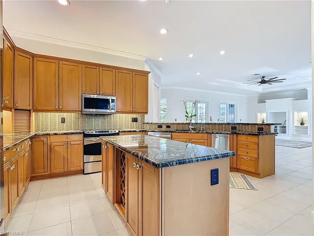 Kitchen featuring ornamental molding, light tile patterned flooring, brown cabinets, tasteful backsplash, and dark stone countertops