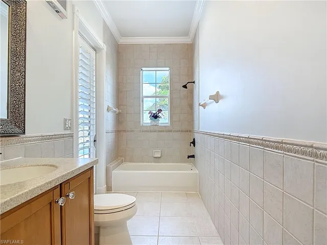 Full bathroom with tile walls, vanity, bathing tub / shower combination, light tile patterned flooring, and a wainscoted wall