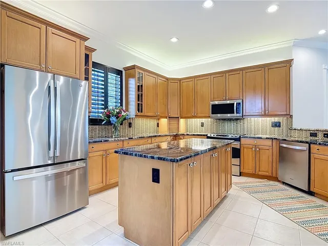 Kitchen with appliances with stainless steel finishes, ornamental molding, glass insert cabinets, decorative backsplash, and dark stone counters