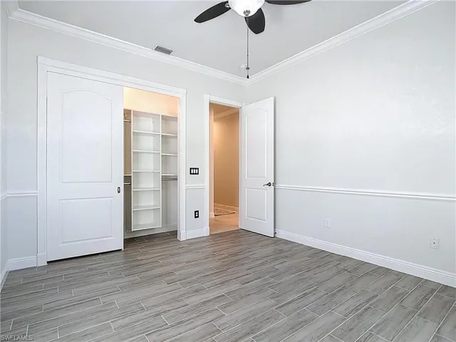 Unfurnished bedroom with ornamental molding, wood tiled floors, and ceiling fan
