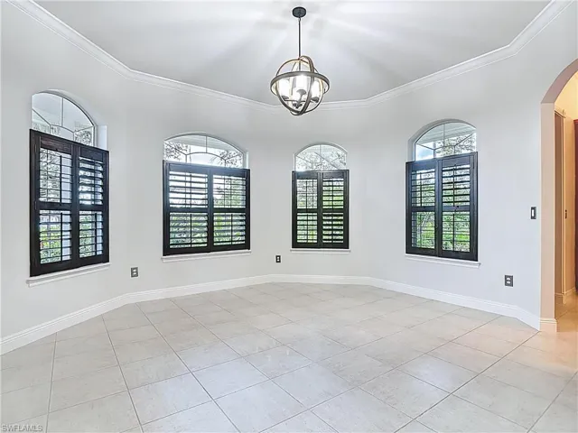 Empty room featuring crown molding, arched walkways, a chandelier, and light tile patterned floors