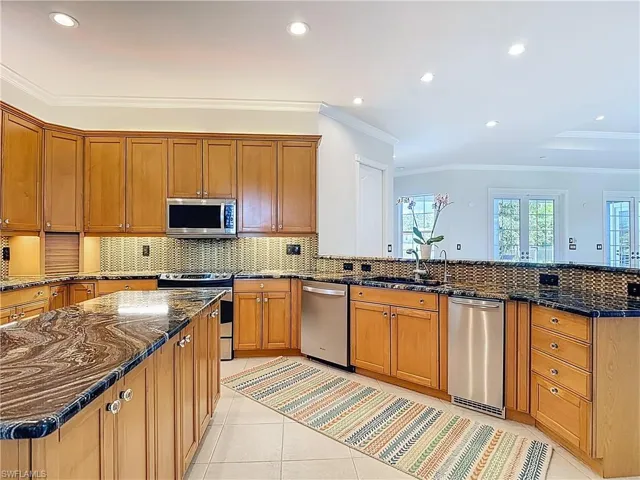 Kitchen with crown molding, dark stone counters, brown cabinets, tasteful backsplash, and appliances with stainless steel finishes
